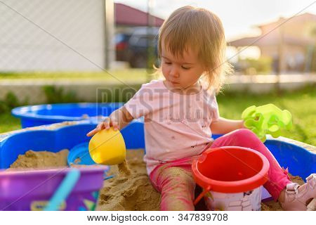 Baby Girl Playing In A Sandbox Outdoors In Sunny Day. Child In Blue Sandbox In Summer.