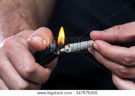Close Up Of A A Mans Hands With A Rolled Marijuana Joint And Lighting It With A Lighter