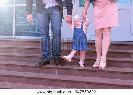Baby Girl Learning To Go Holding Parents Hands Going Down Steps. Mom And Dad Teachin Ther Daughter T