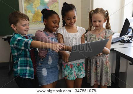 Front view of a group of happy and smiling schoolkids studying standing on digital tablet in classroom of elementary school