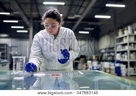 Laboratory brunette girl with flask with blue liquid in her hands checks quality
