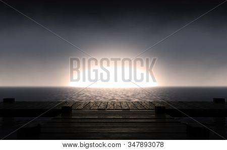 A Wooden Boat Jetty Jutting Out Across Calm Water With The Sun Rising On The Horizon In Dim Light - 