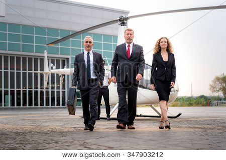 Three Businessman And Businesswoman Manager With Briefcase Walking From Helicopter When He Arrive De