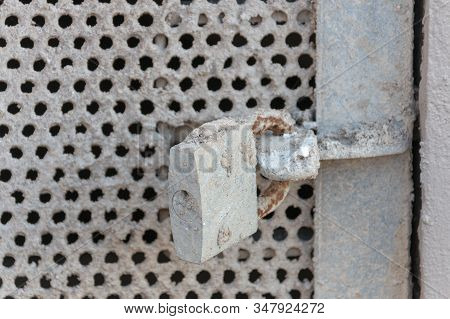 A Close Up View Of A Locked Metal Meshed Door Leading To A Passway Under A Building. Covered In Conc