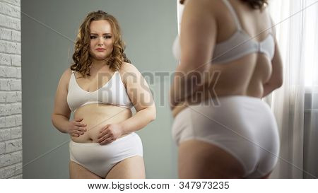 Unhappy Overweight Lady In Underwear Looks In Mirror, Ashamed Of Excess Weight