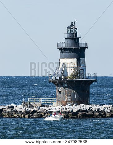 People Are In A Small Boat Fishiing Infront Of The Orient Point Lighthouse On A Windy Day.