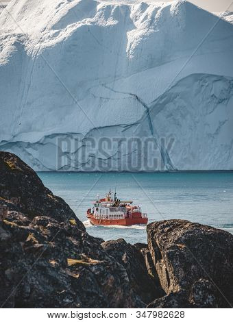Orange Whale Watching Tour Boat Ship With Icebergs In Background. View Towards Icefjord In Ilulissat