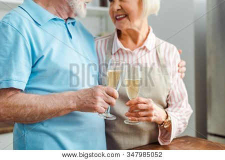Cropped View Of Senior Couple Smiling At Each Other While Clincing With Champagne In Kitchen