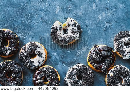Flatlay Of Dark And White Chocolate Frosted Donuts With Crumbled Creme Filled Cookies Over A Blue Te