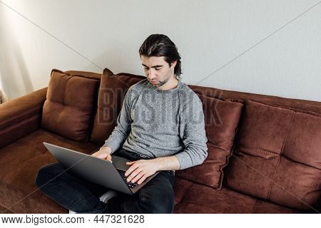 Young Caucasian Boy Student Studying At Home Reading Compendium Notes In Exercise Book Using Laptop 