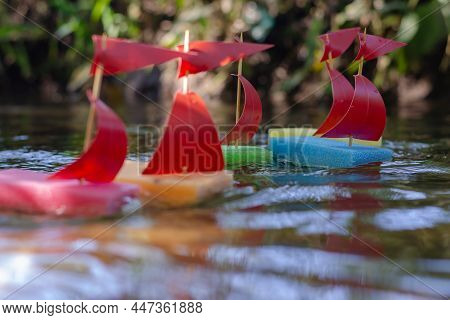 A Group Of Children's Toy Ships Are Floating In A Stream. Five Homemade Mast Boats Floating On The S