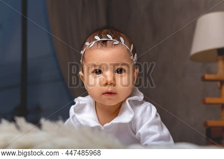 Little Baby Girl In White Bodysuit And Headband Standing On All Fours. Looking To The Camera. Baby S