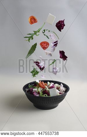 Healthy Eating Concept - Salad Pourig Into Black Bowl Against Light Background. Image Contains Copy 