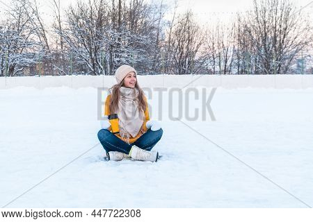 Portrait Of Happy Young Woman In Yellow Sweater And Ice Skates Sitting On The Snow And Holding Mug W