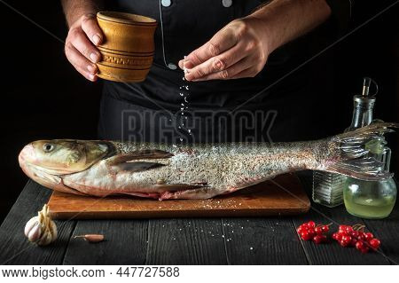 Professional Cook Prepares Silver Carp Herring In The Restaurant Kitchen. The Cook Sprinkles Salt On