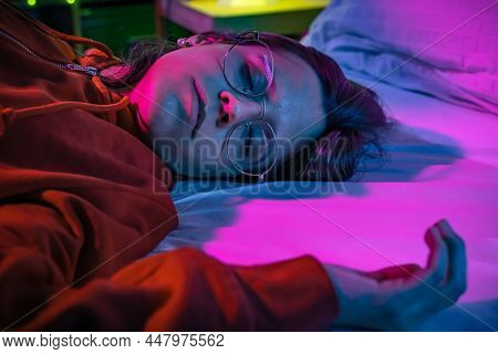 Top View Of A Beautiful Girl Sleeping Cozily On A Bed In Her Night Room With Colorful Neon Lights.