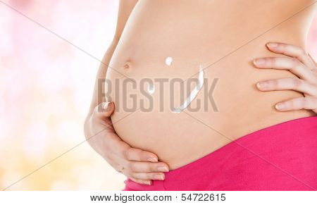pregnancy, maternity and health concept - belly of a pregnant woman with cream and smile symbol