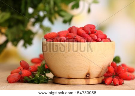 ripe barberries in wooden bowl with green leaves, on table