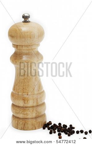 Side view of a peppermill standing next to a scattering of peppercorns, over white.