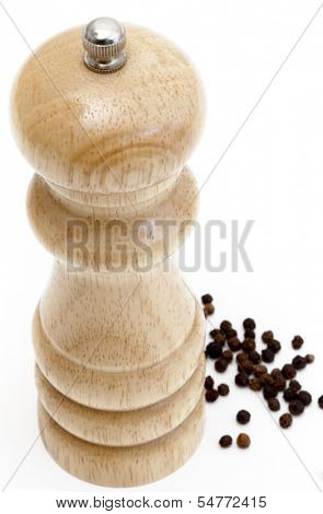 High angle view of a peppermill standing next to a scattering of peppercorns, over white.