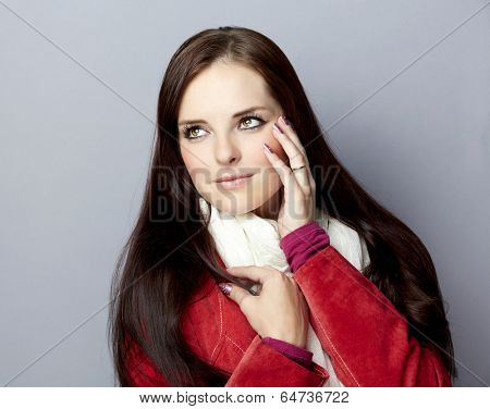 Portrait of a young smiling casual woman with long brunette hair on gray studio background, wearing red suede leather jacket and white scarf 