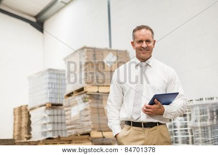 Manager standing with hand in the pocket holding tablet pc in a large warehouse