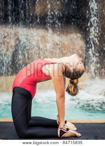Woman practicing yoga near waterfall. Camel Pose. Ustrasana