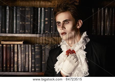 Handsome vampire nobleman studying ancient books in the library. Halloween. Dracula costume.