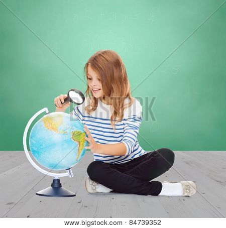 education, childhood, geography and school subject concept - happy little student girl looking at globe with magnifier over green chalk board background