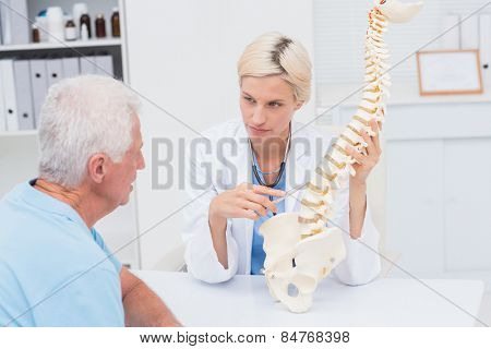 Female doctor explaning spine model to senior male patient in clinic