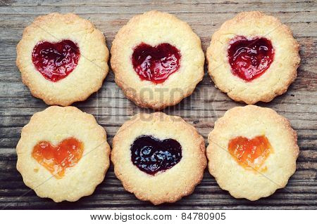 Homemade cookies with heart shaped jam on wooden table