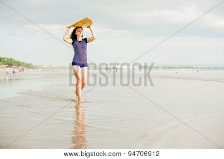 Beautiful sexy surfer girl on the beach at sunset walks along ocean shore, yellow surfboard in her h