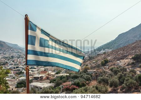 Flag of Greece waving at Pothia cityscape the capital of Kalymnos island background