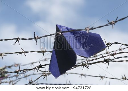 Refugee Labeled Passport Folded As A Paper Plane Hanging In A Barbed Wire