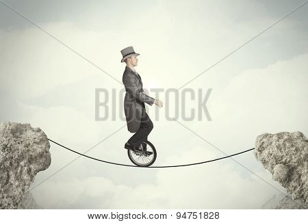 Brave business man riding an mono cycle between cliffs concept