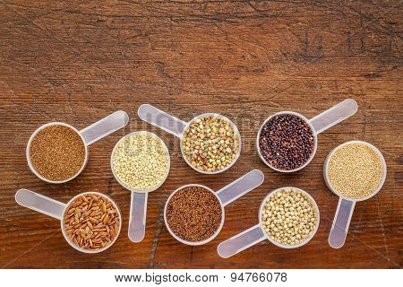 gluten free grains (quinoa, brown rice, kaniwa, amaranth, sorghum, millet, buckwheat, teff) - a set of measuring scoops on a rustic wood with a copy space