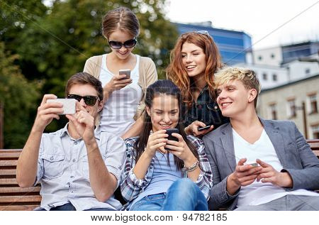 summer, technology, education and teenage concept - group of happy students or teenagers with smarphones taking selfie and texting messages at campus