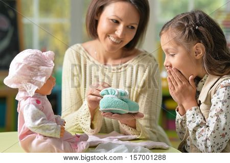 Portrait of happy mother and her cute daughter play with baby doll together