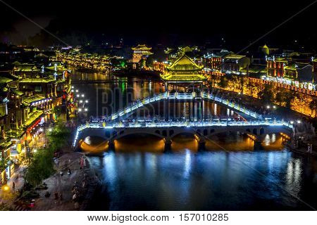 Illuminated Fenghuang Bridge Over Tuojiang River In Downtown Fenghuang, Xiangxi, China At Night