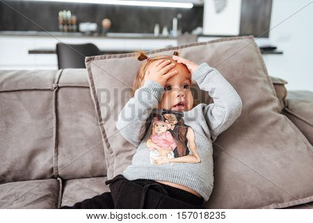Pretty baby on sofa. hends on head. looking away