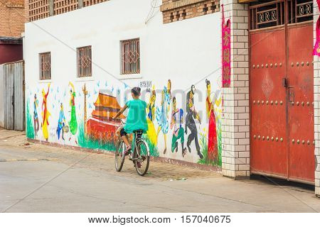 Girl Passing Painted Wall In Turpan, China