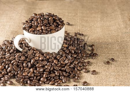 Roasted coffee bean in white cup place on hemp sack