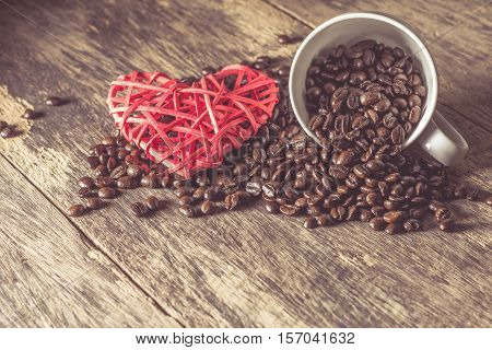Spilled of coffee beans in white cup on wooden table and heart icon