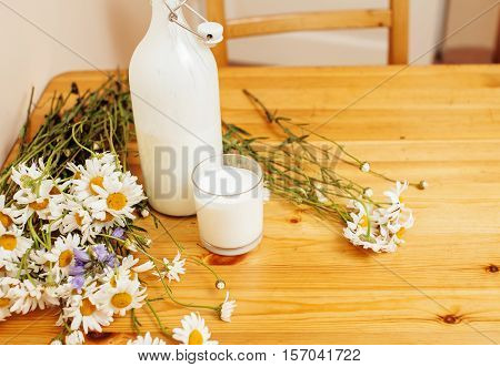 Simply stylish wooden kitchen with bottle of milk and glass on table, summer flowers camomile, healthy foog moring concept noone close up