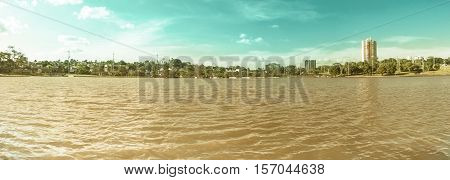 Day at park with a lake green vegetation and some buildings of the city on background. Scene reflected on water. Panoramic photo at Parque das Nações Indígenas in Campo Grande MS Brazil.