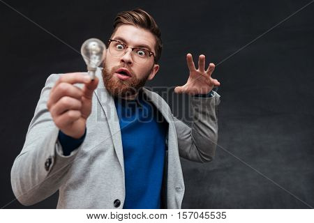Surprised funnny bearded man in eyeglasses lights the bulb over black backgorund