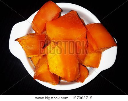 Slices of pumpkin with sugar baked in the oven. The white plate on a black background