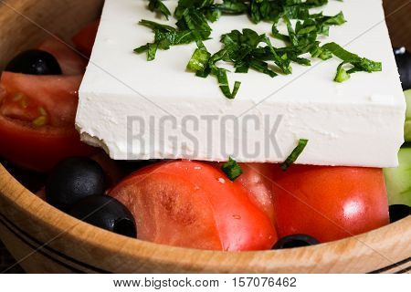 Greek salad with feta cheese and vegetables on wooden plate