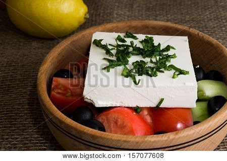 Greek salad with feta cheese and vegetables on wooden plate
