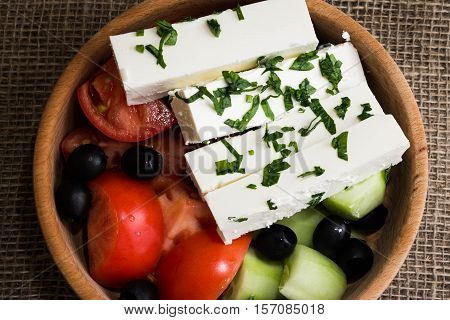 Greek salad with feta cheese and vegetables on wooden plate